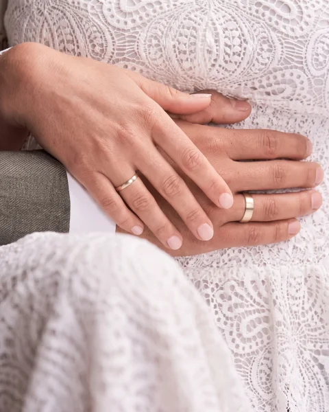 Zwei Hände mit Trauringen vor einem Spitzenkleid