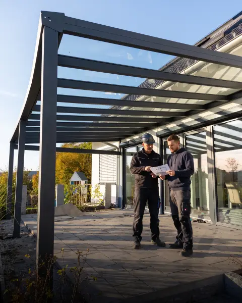Montagefachkräfte besprechen einen Bauplan unter einer Terrassenüberdachung